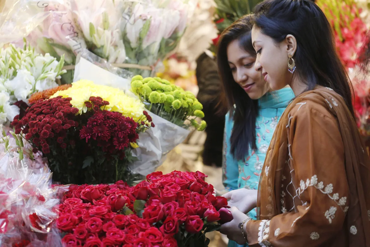 Two women browsing and choosing colorful bouquets at an outdoor flower market