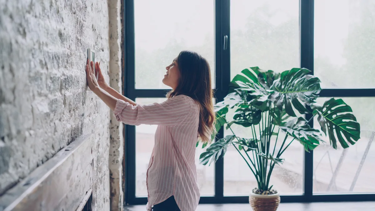 Woman adjusting a smart thermostat on the wall in a modern living room