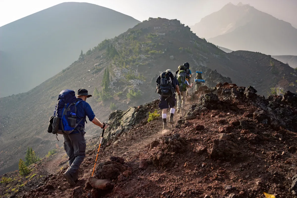 Two backpackers with large hiking packs walking a mountain trail at sunrise