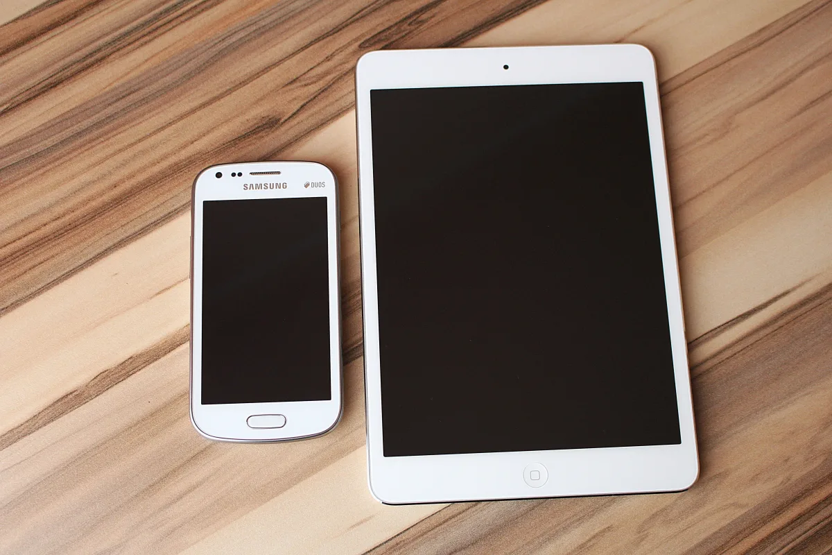 White smartphone and tablet side by side on a wooden table for size comparison