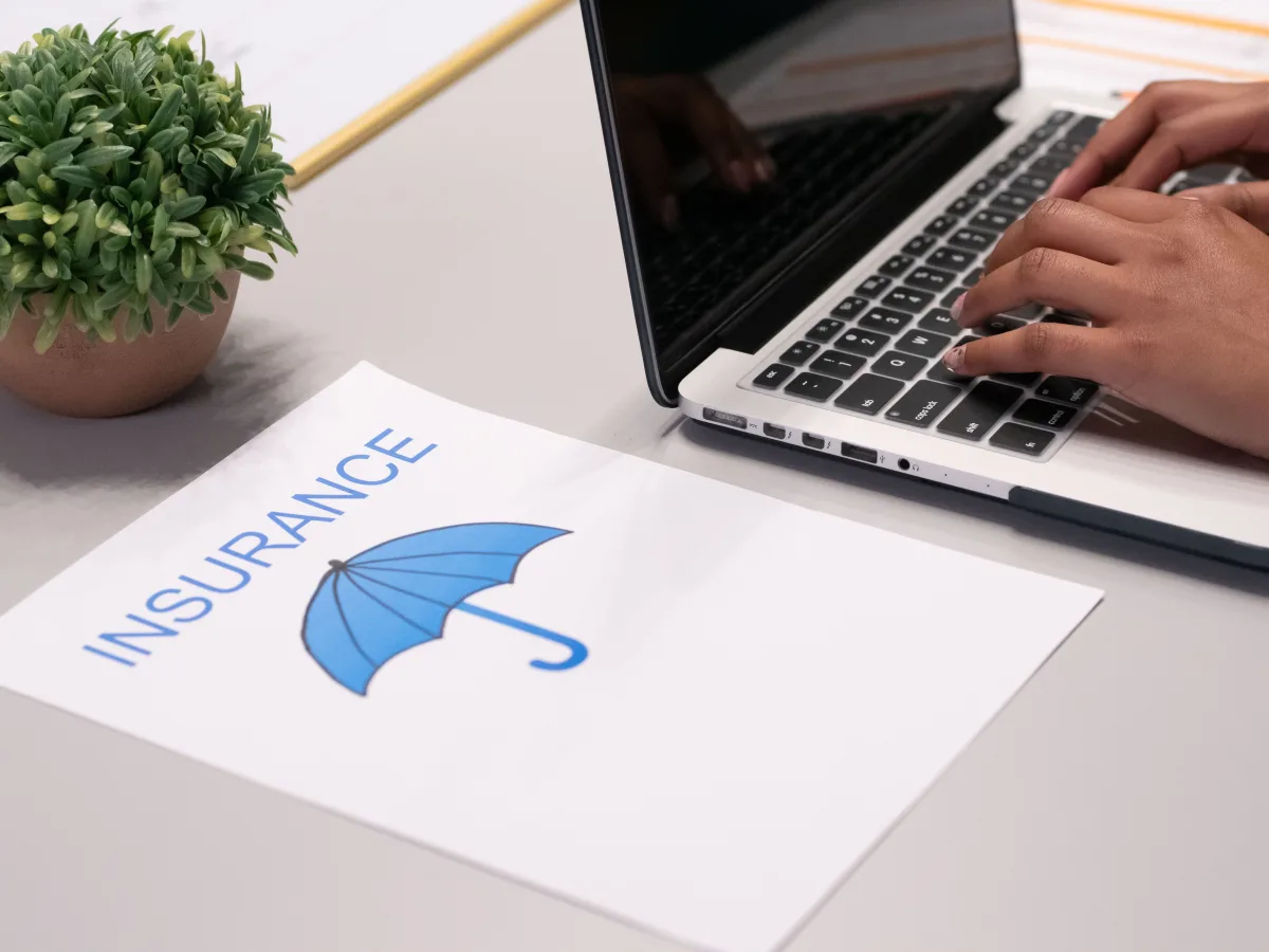 Hands typing on laptop reviewing insurance contract on desk