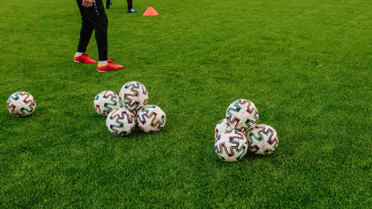 Pile of soccer balls on green field during training session