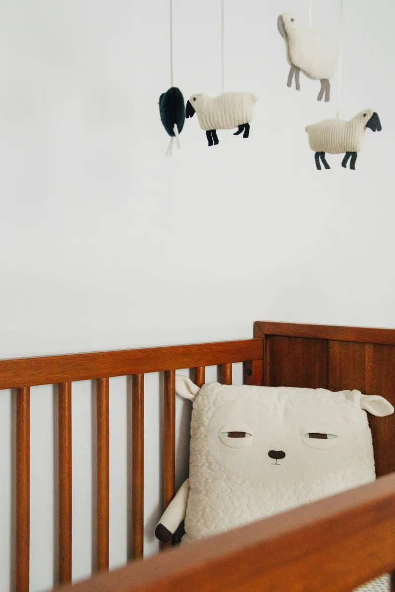 Convertible crib with sheep pillow and hanging mobile in a cozy nursery