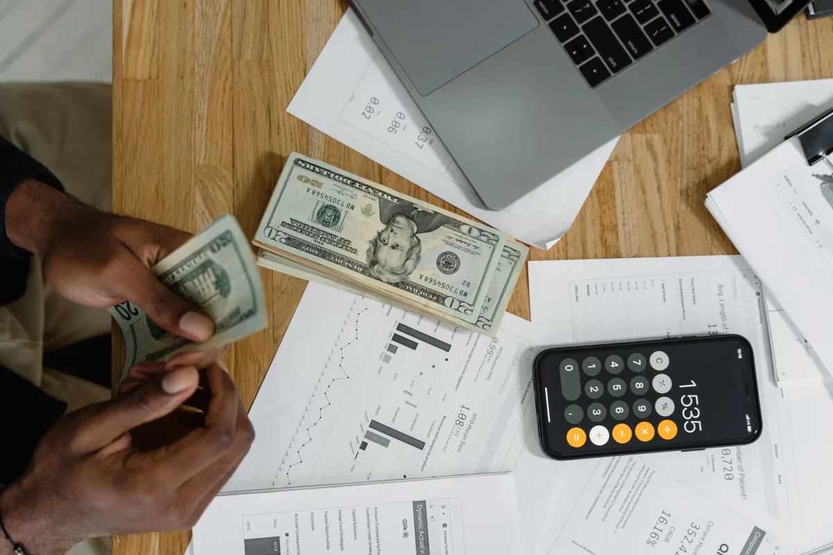 Person counting cash on desk with calculator and laptop — personal finance management