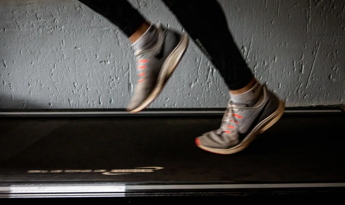 Person in black pants wearing Nike sneakers running on treadmill