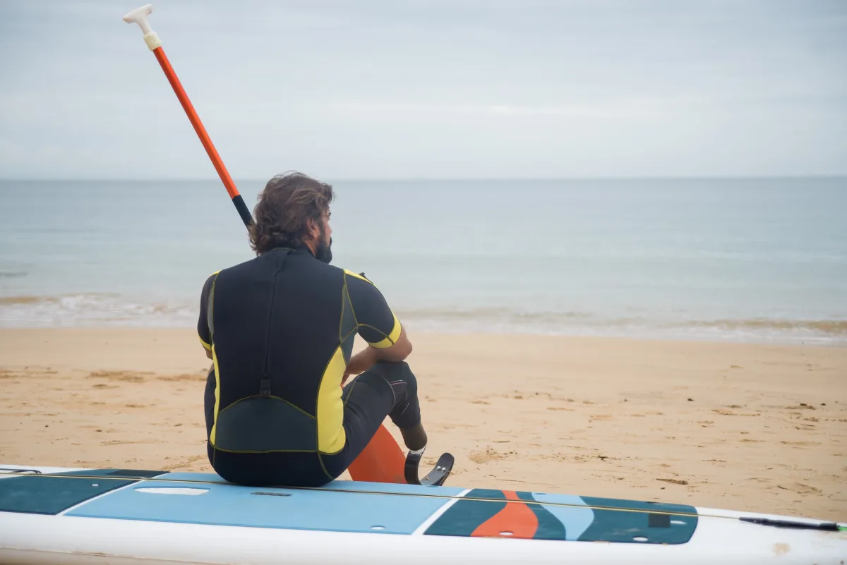 Person with a life jacket sitting on a paddleboard at a calm beach