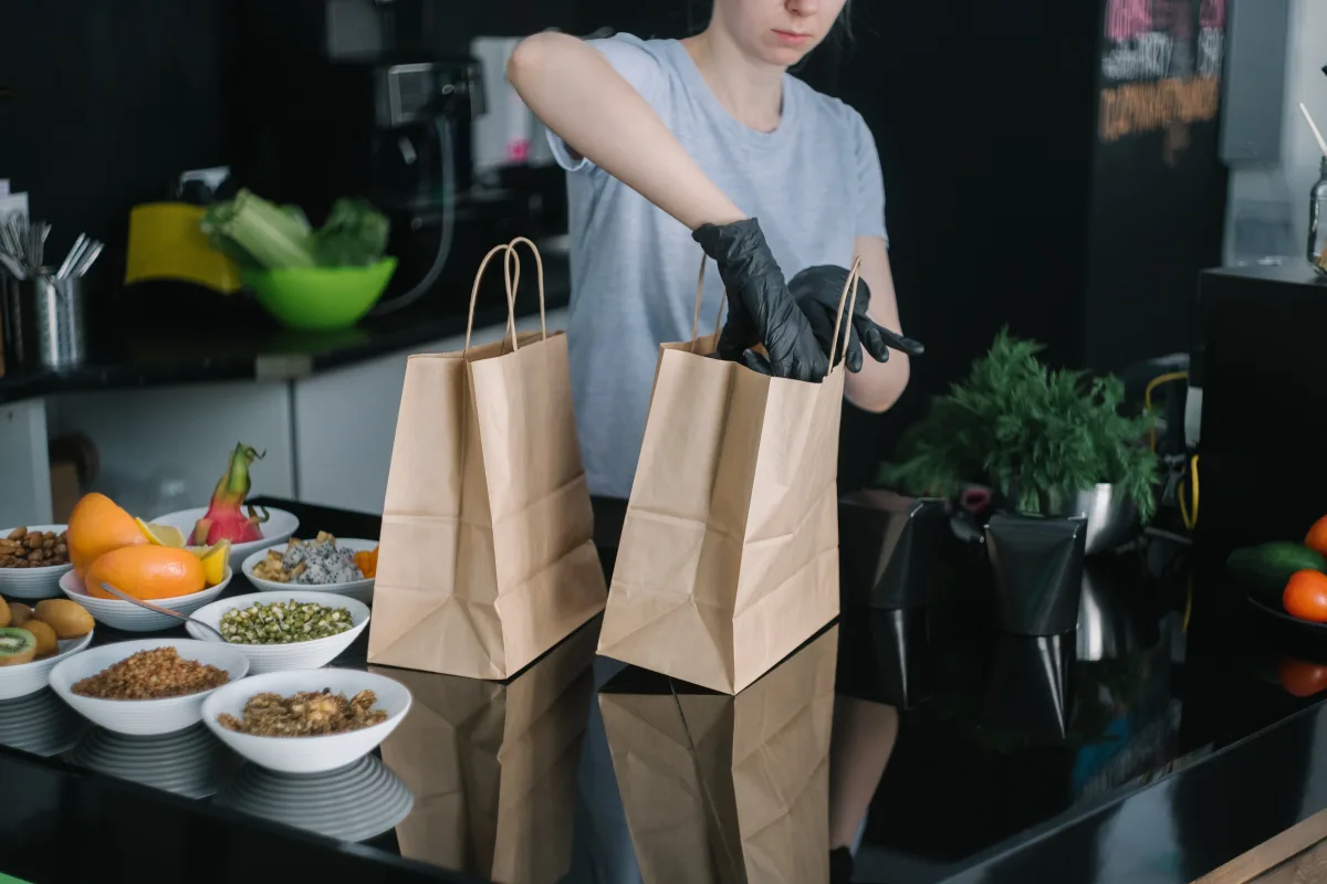 Person packing fresh food ingredients into paper bags in a commercial kitchen