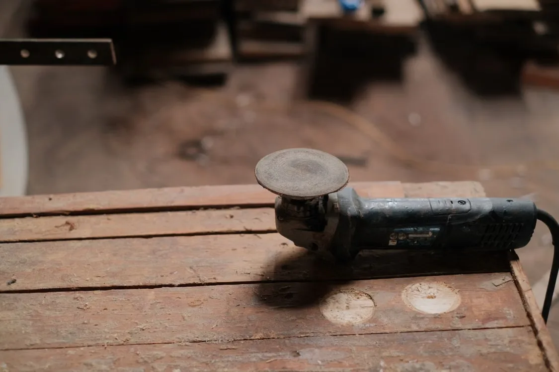 Electric angle grinder resting on a wooden workbench in a rustic workshop