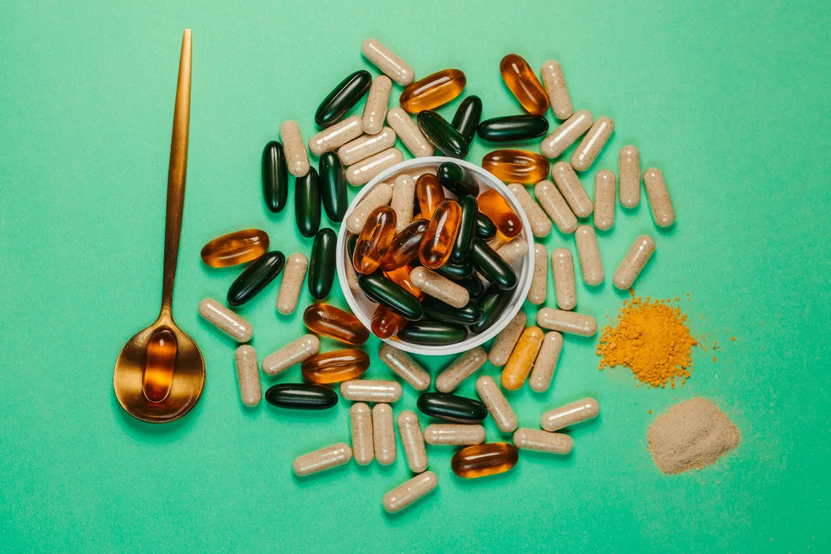 Colorful capsules and powder with golden spoon on green background