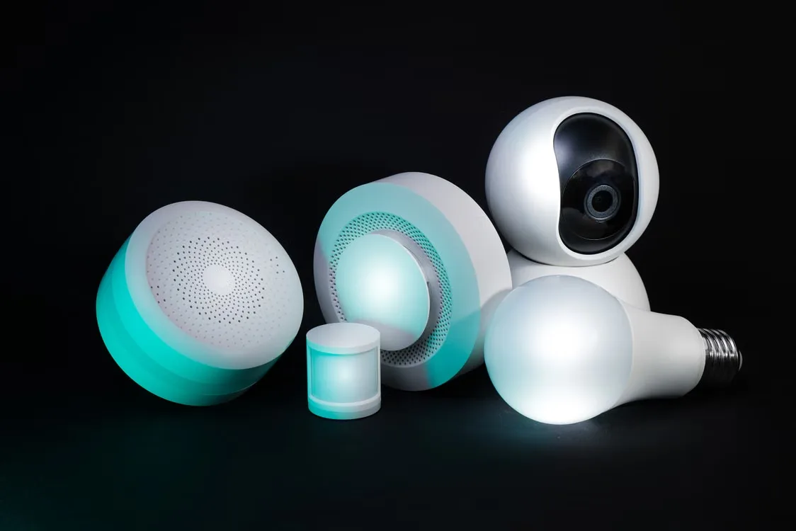 Collection of smart home devices including camera, bulbs, and sensors on dark background