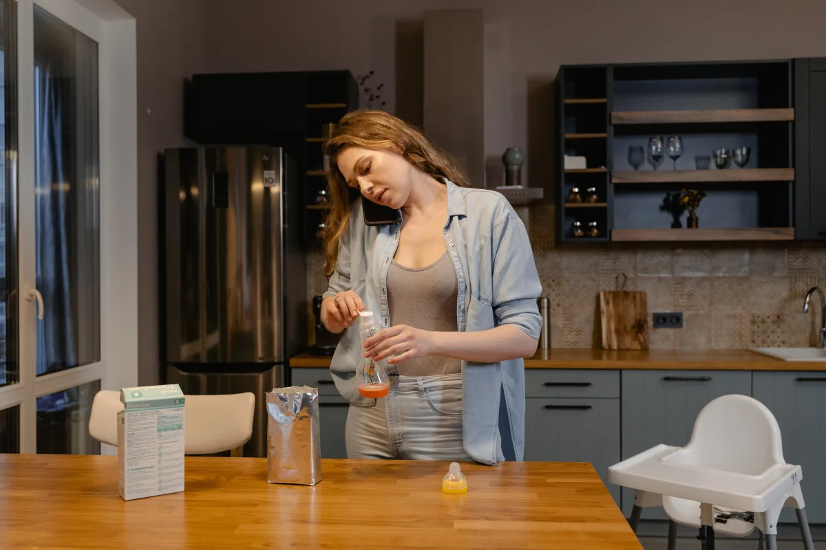 Mother multitasking while preparing baby formula in a modern kitchen