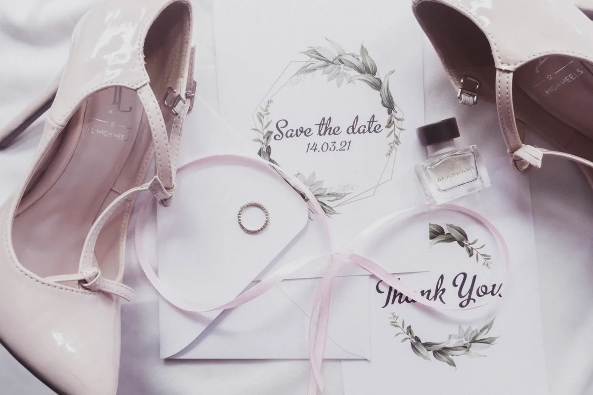 Flat lay of wedding heels, perfume, and invitation suite on a marble surface