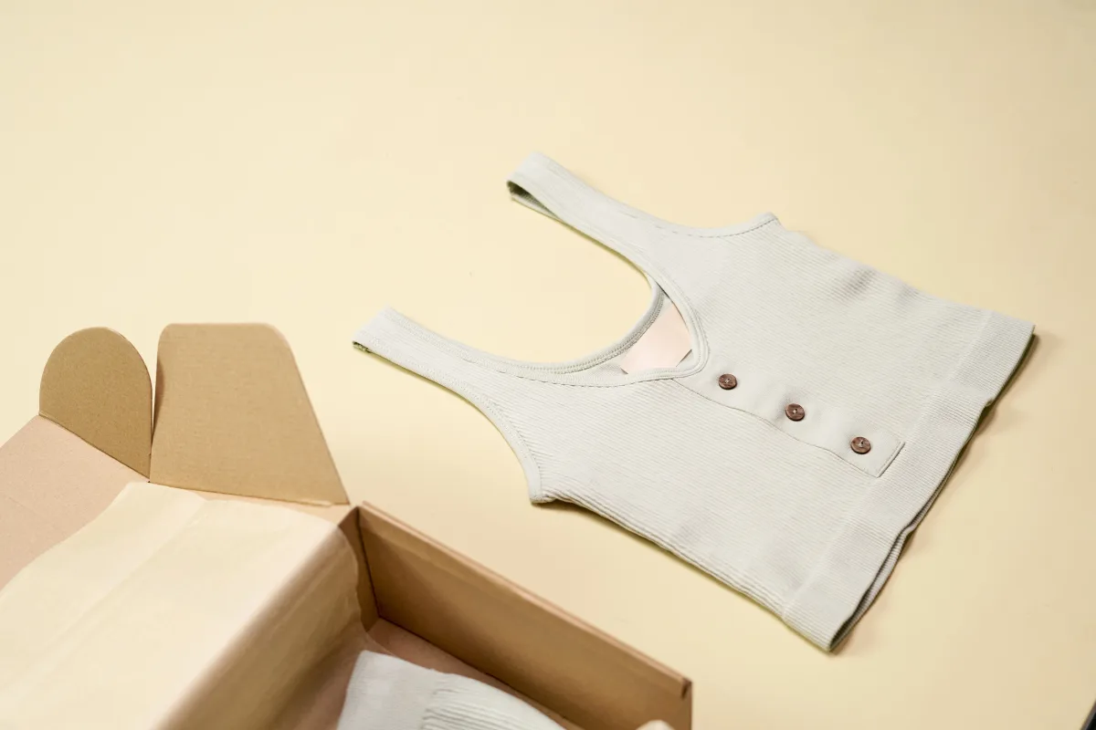 Minimalist flatlay of a folded sleeveless top next to an open cardboard subscription box