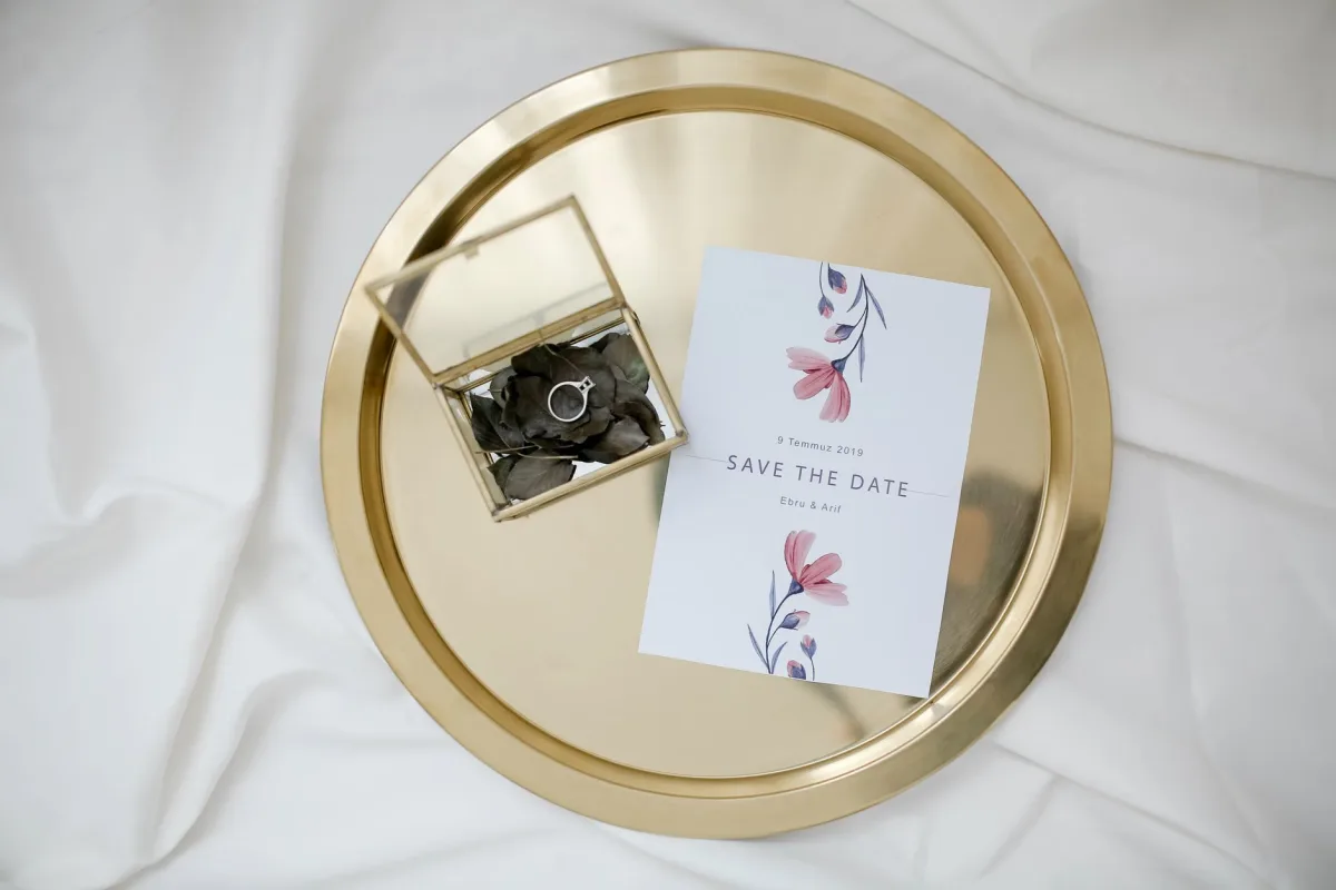 Save-the-date card and engagement ring displayed on a gold tray
