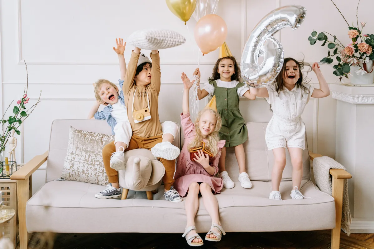 Happy kids celebrating with balloons on a living room sofa
