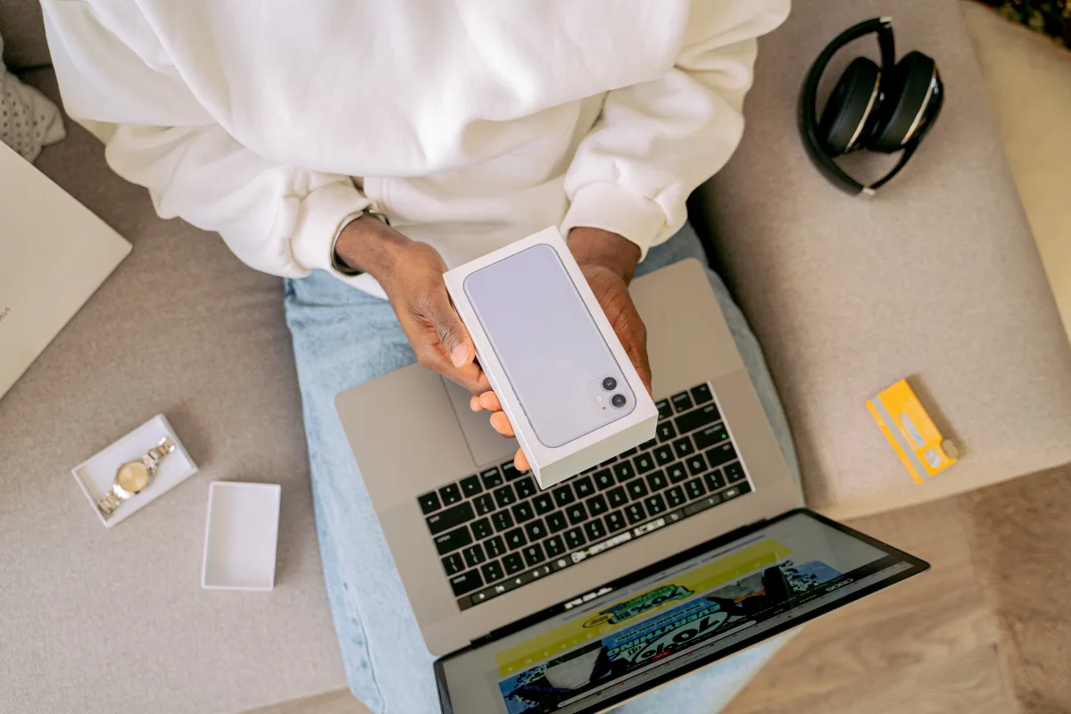 Person unboxing a new smartphone next to a laptop on a sofa