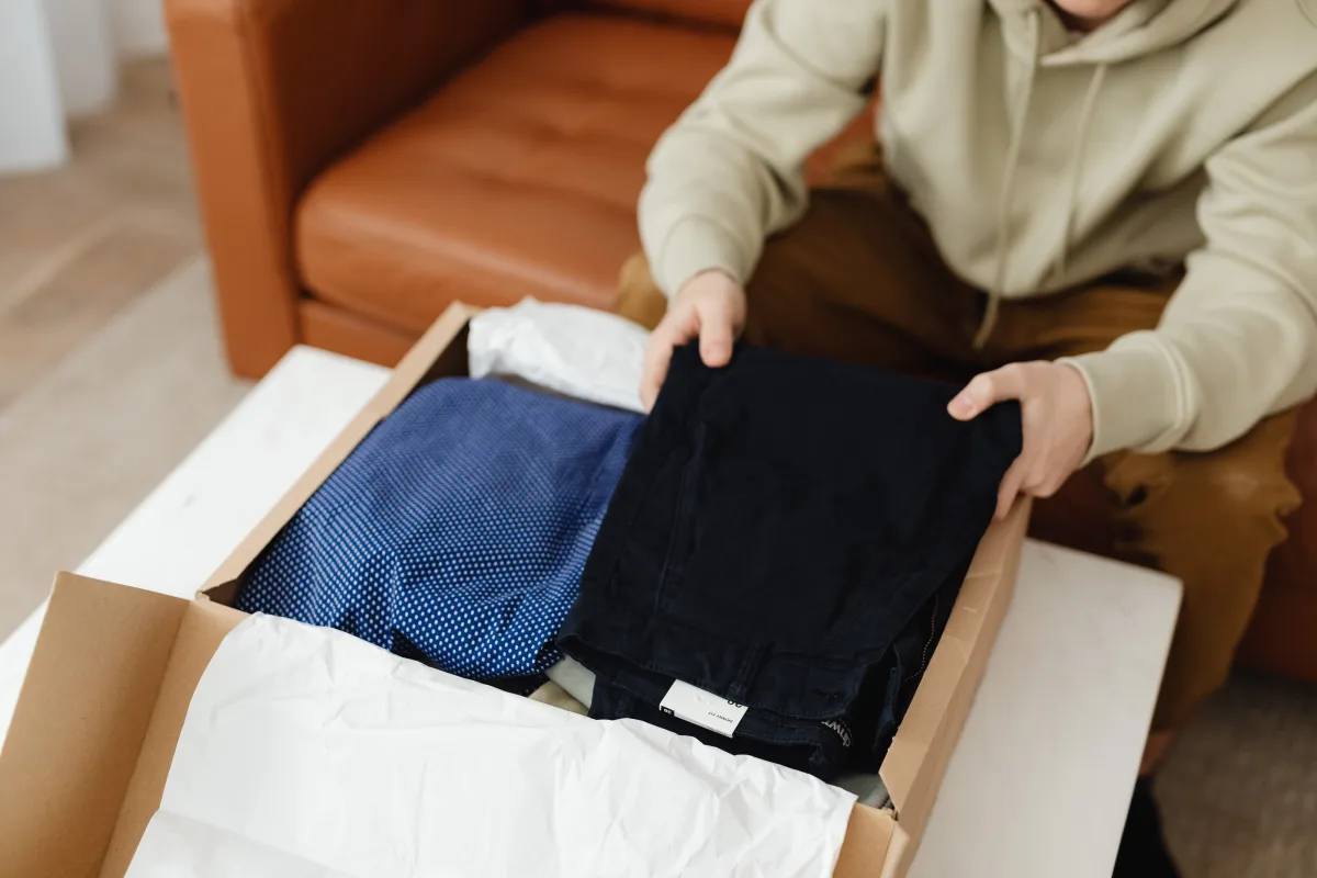 Man unboxing new clothes from a delivery box on a table indoors