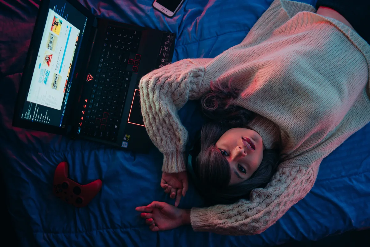 Teen lying on bed with laptop and game controller — best budget gaming laptops under 1500 dollars 2026