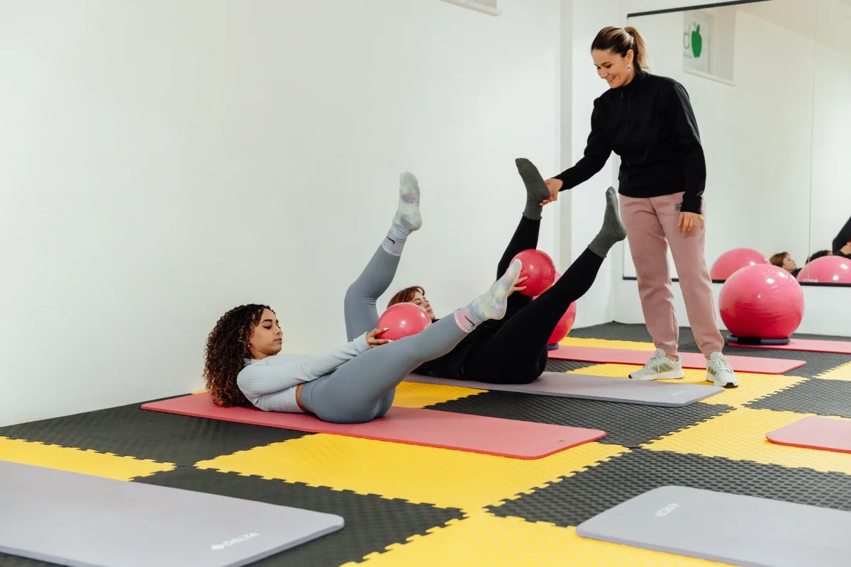 Women engaged in Pilates class using pink balls and yoga mats at a gym