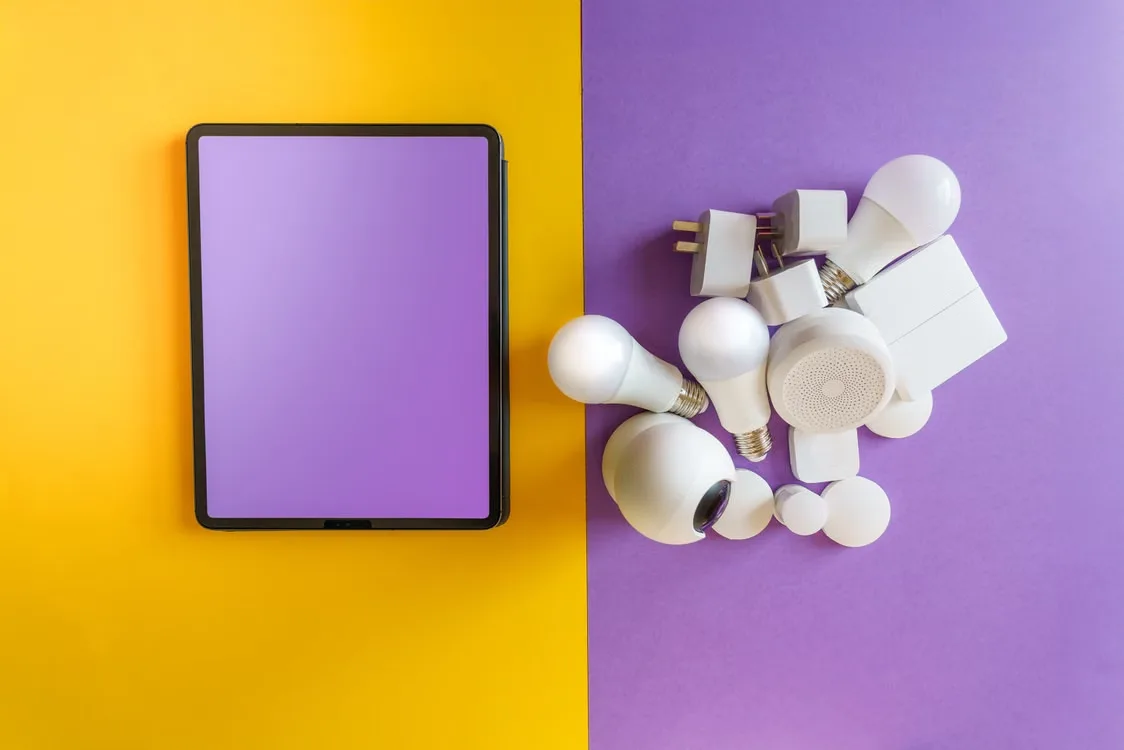 Smart home devices arranged beside a blank tablet on colorful yellow and purple background