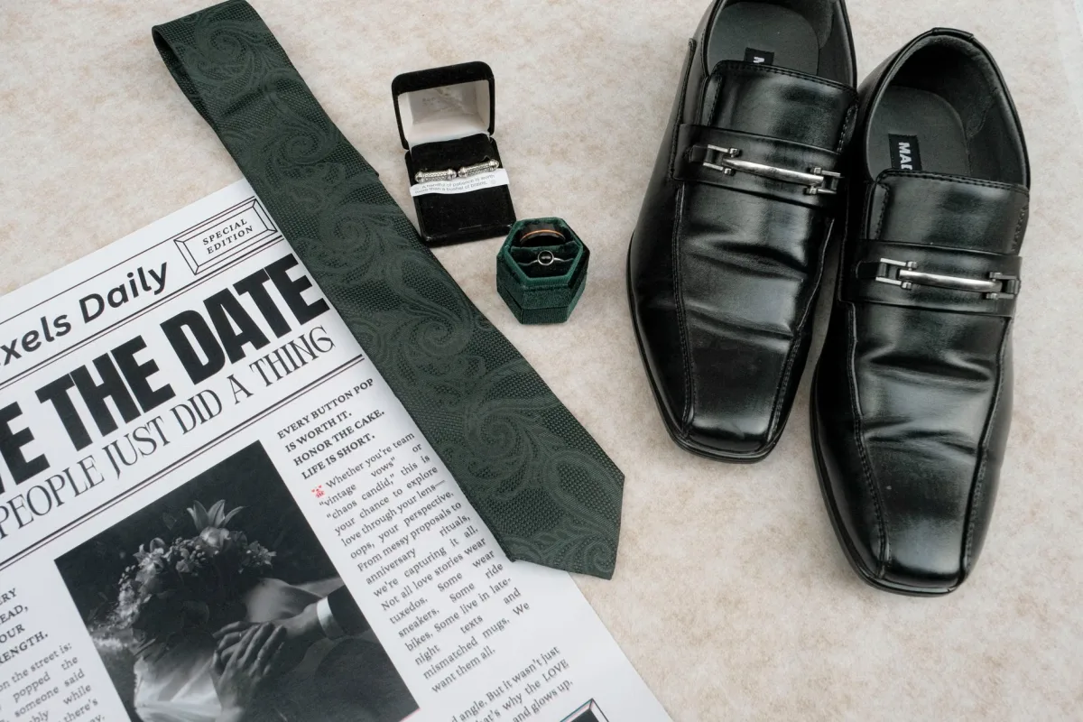 Wedding flat lay with dress shoes, tie, newspaper, and rings