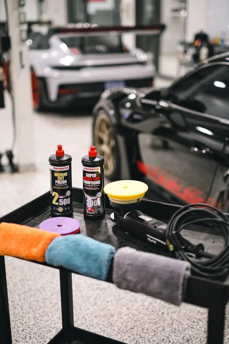Car detailing products + buffer on table near sports cars