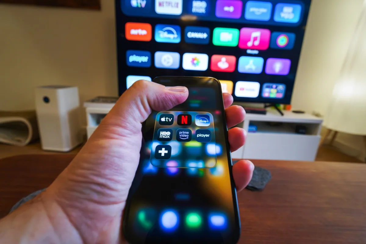 Person holding phone with streaming app icons in front of a smart TV