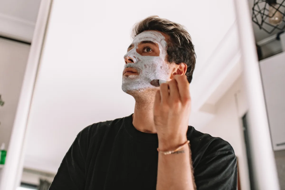 Man applying face mask in bathroom mirror as part of skincare routine