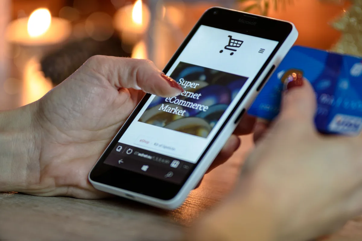 Person checking phone and laptop while shopping online — illustrating price comparison behavior