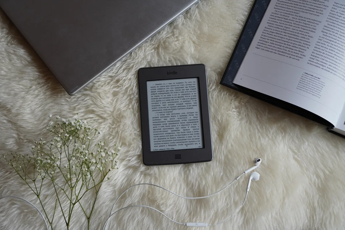 Flat lay of an e-reader, flowers, and earphones on a cozy surface
