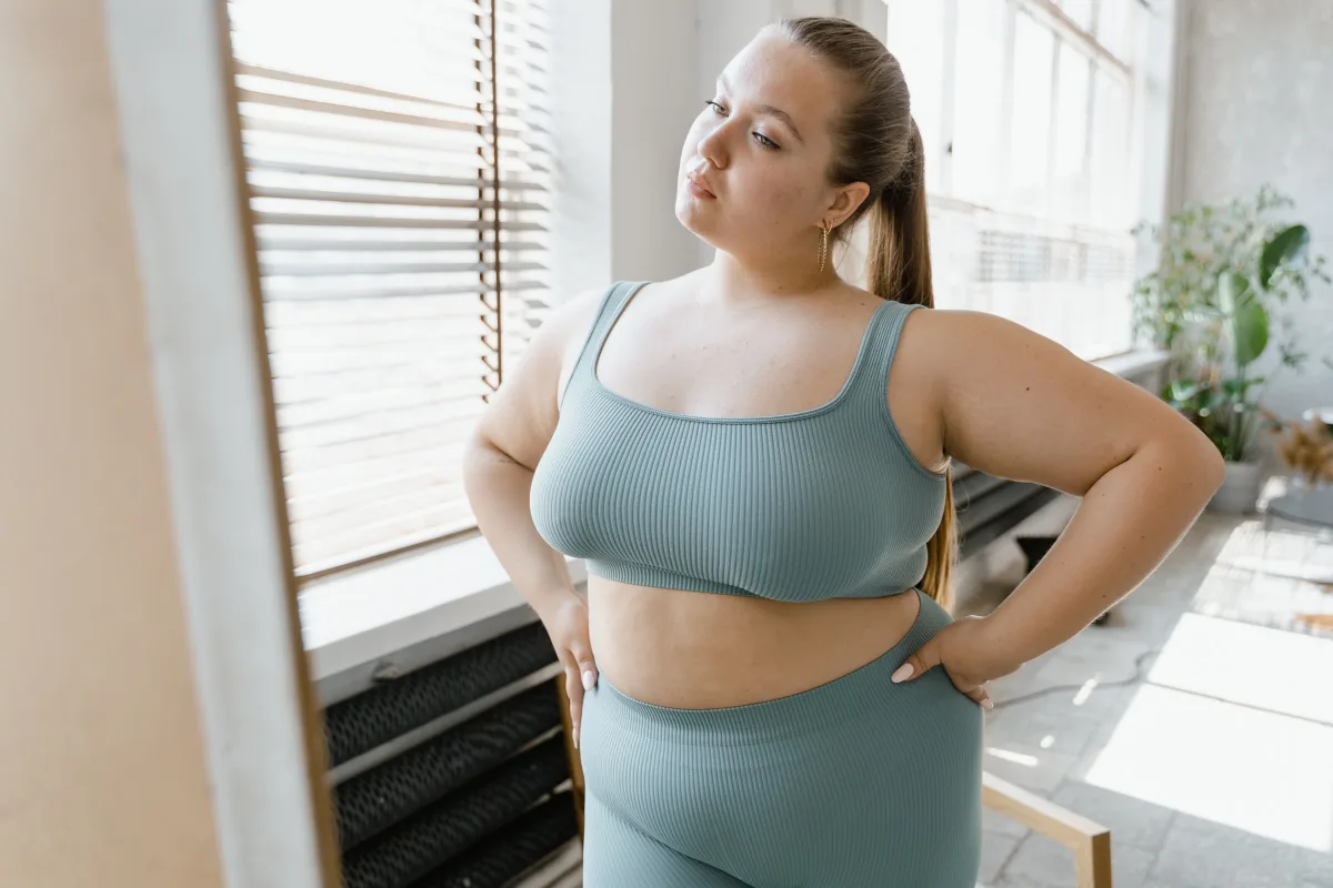 Plus-size woman in activewear poses confidently indoors with hands on her waist