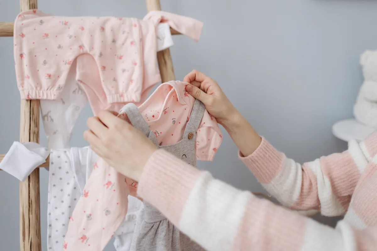 Mother organizing baby clothes on a wooden nursery rack