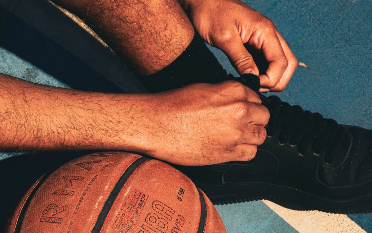 Person tying basketball shoe on sunlit outdoor court