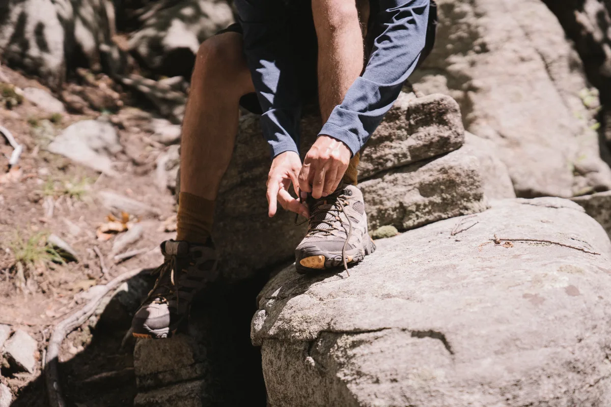 Hiker lacing boots on rocky trail before descent