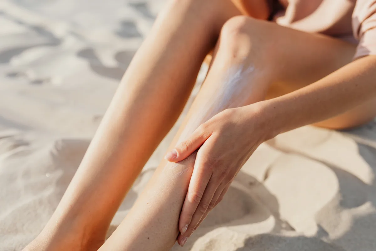 Close-up of applying sunscreen on legs on sunny beach sand