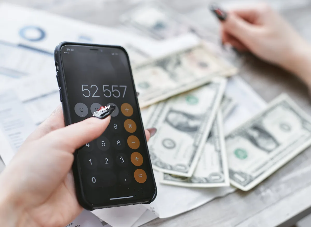 Person using smartphone calculator next to dollar bills — budgeting app comparison 2026