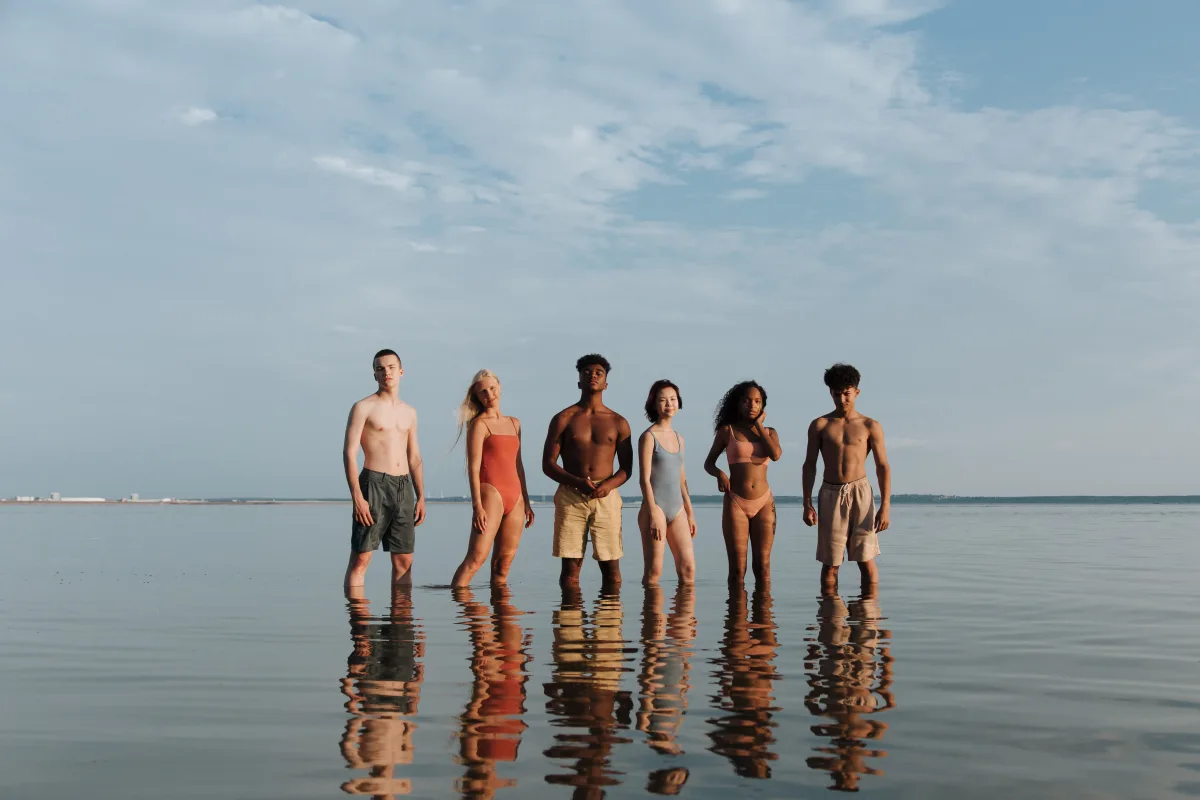 Group of young adults wading in ocean wearing swimwear at beach