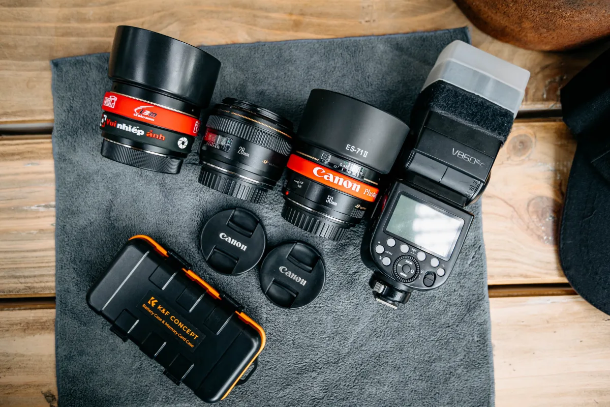 Flat lay of camera lenses, flash, and accessories on wooden table