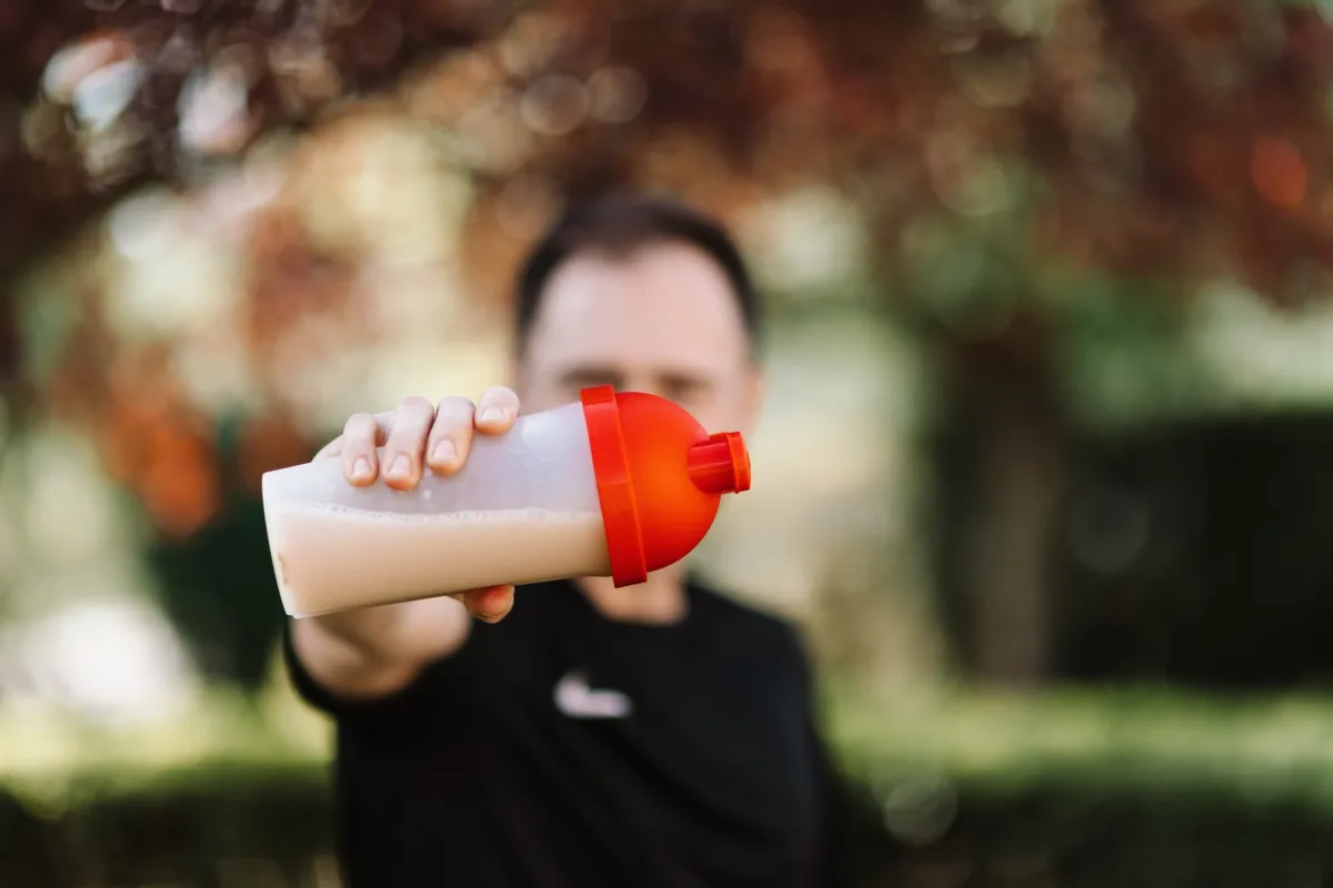 Man holding plastic protein shake tumbler outdoors