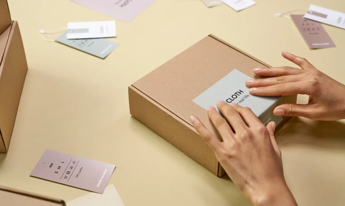 Hands carefully packaging clothing in a cardboard box with eco-friendly tags