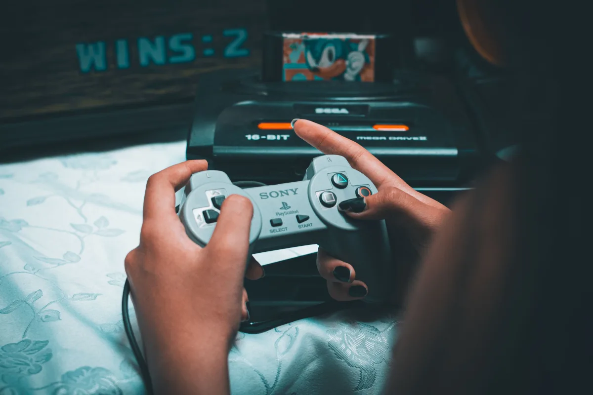 Close-up of hands holding a vintage Sony controller with Sega Mega Drive in the background
