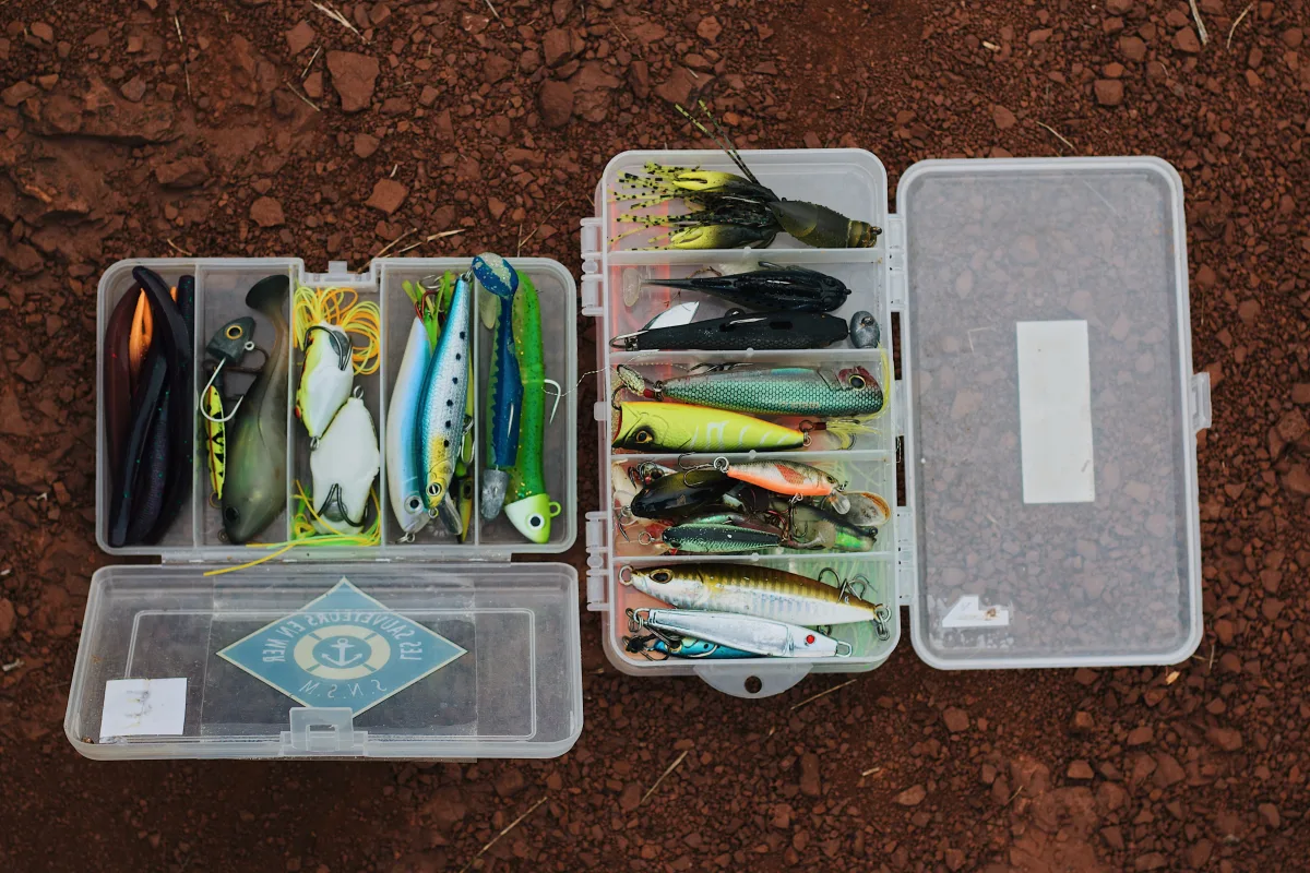 Open tackle boxes with colorful fishing lures on rocky surface outdoors
