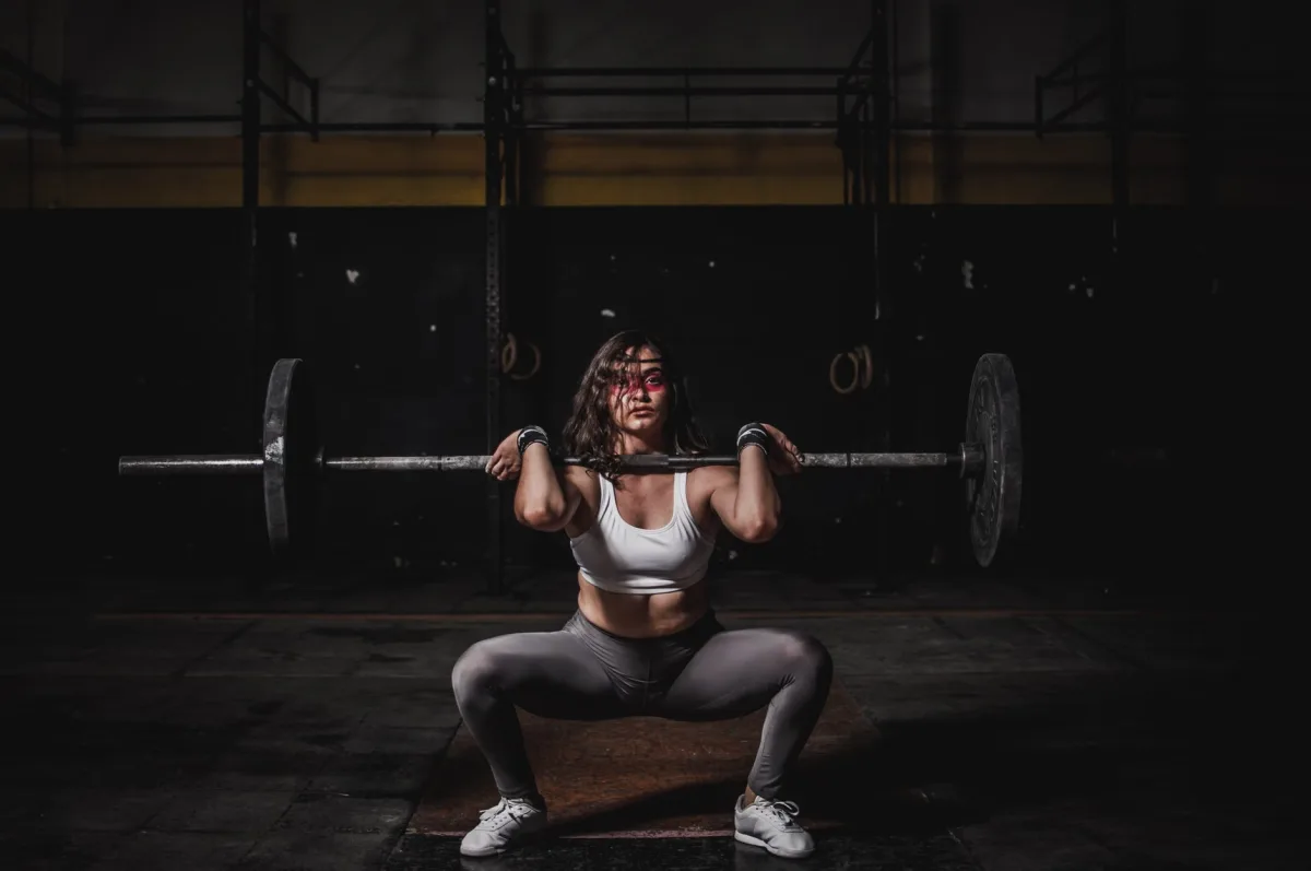 Female weightlifter squatting with barbell in gym