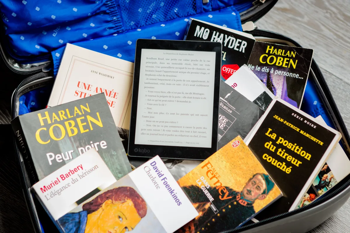 Paperback books and an e-reader packed in an open suitcase for travel