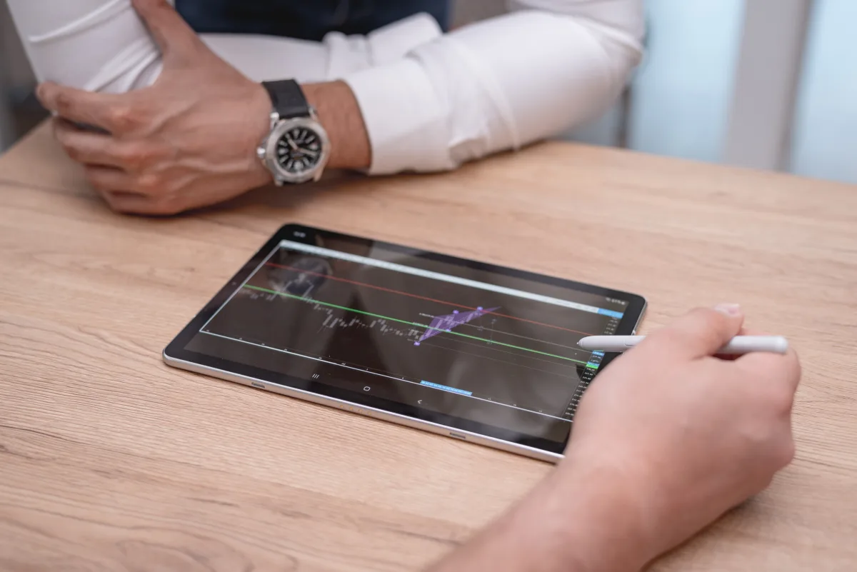 Close-up of hands using a tablet with trading charts on a wooden desk