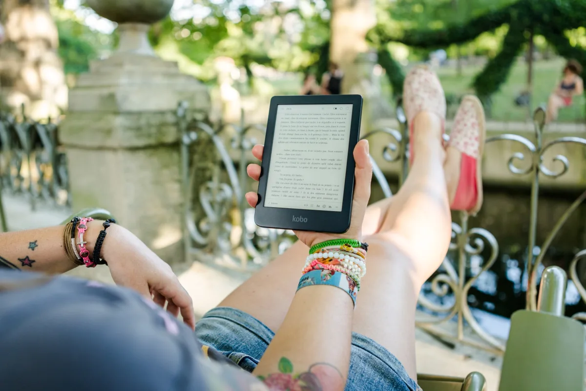 A woman leisurely reading a Kobo e-reader outdoors