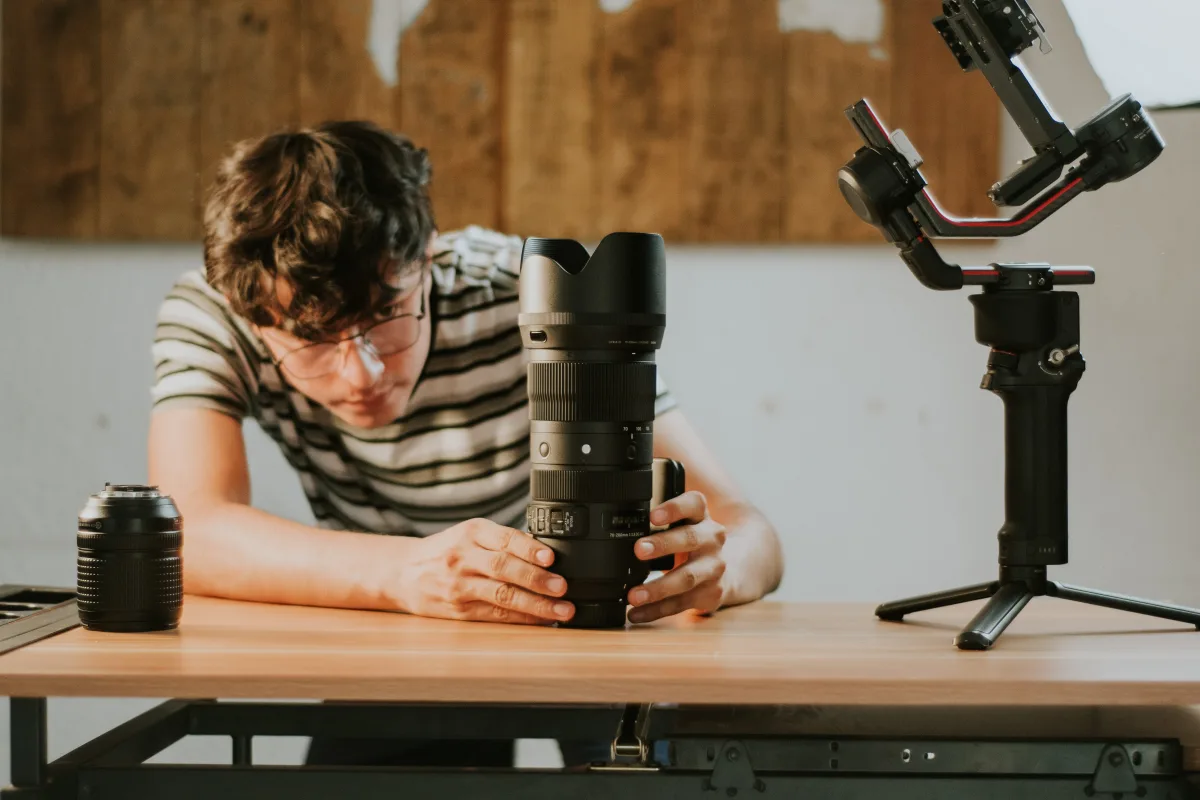 Man examining camera lens on wooden table with photography accessories