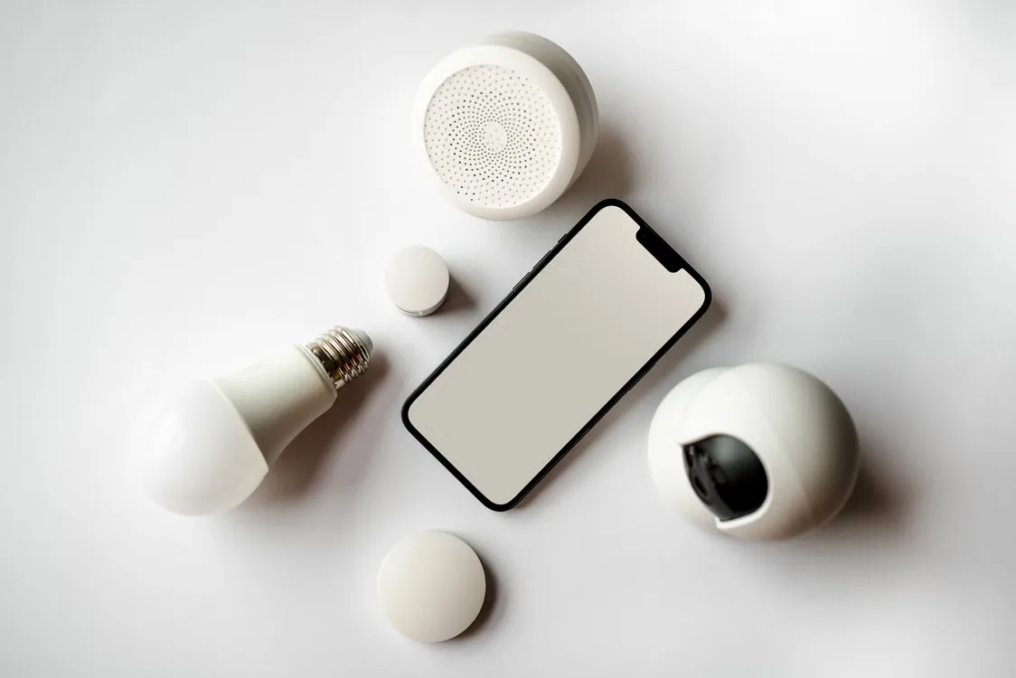 Smartphone and smart home devices flat lay on white backdrop