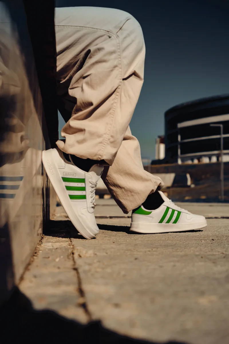 Adidas sneakers with green stripes worn casually on urban sidewalk