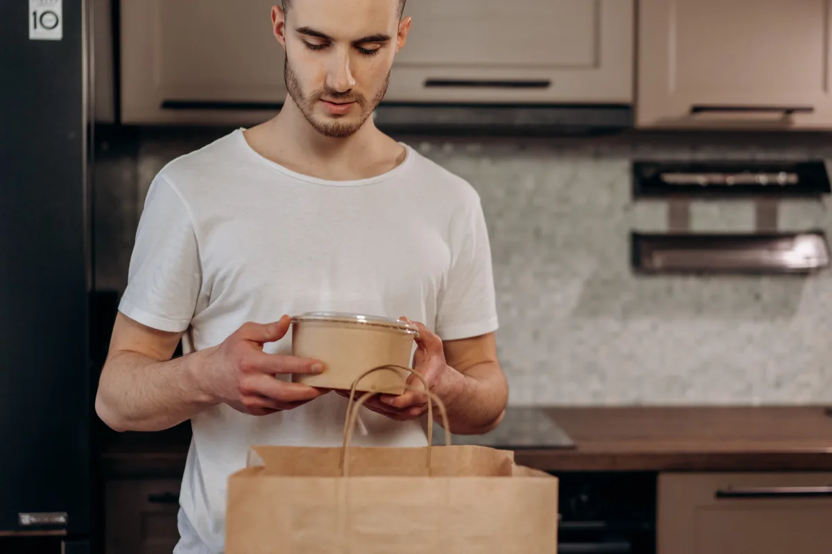 Adult man in a kitchen unpacking food delivery from a paper bag in eco-friendly packaging